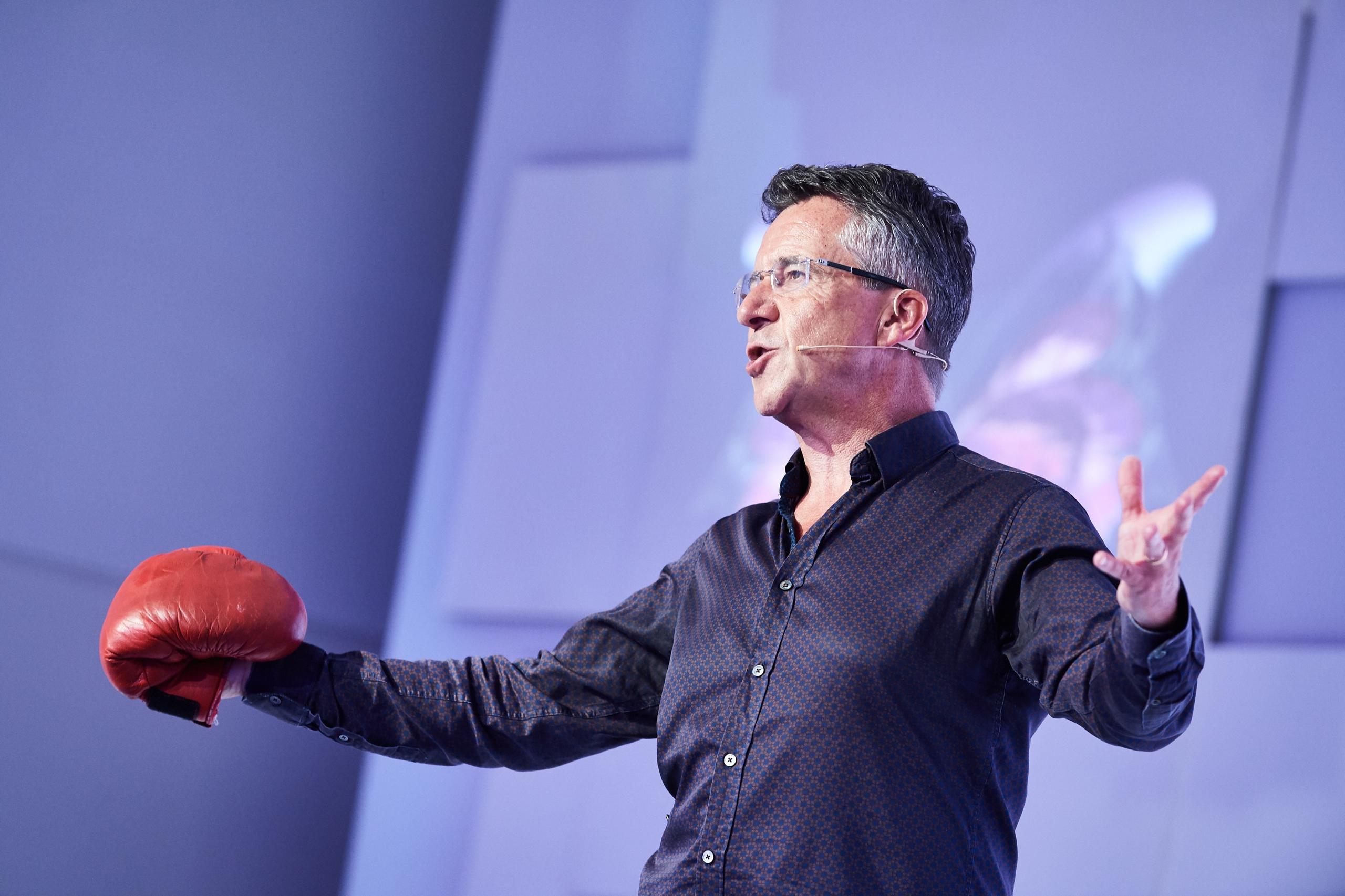 Paul McGee speaking on stage wearing a red boxing glove on one hand