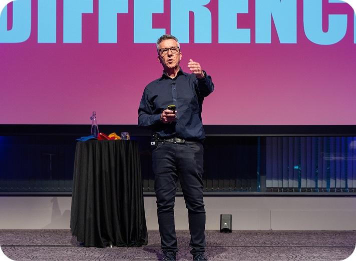 Paul McGee speaking on stage in front of a large screen reading “DIFFERENCE”