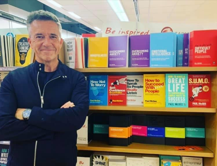 Professor Paul McGee stood next to all of his books on the top shelf in a WH Smiths store