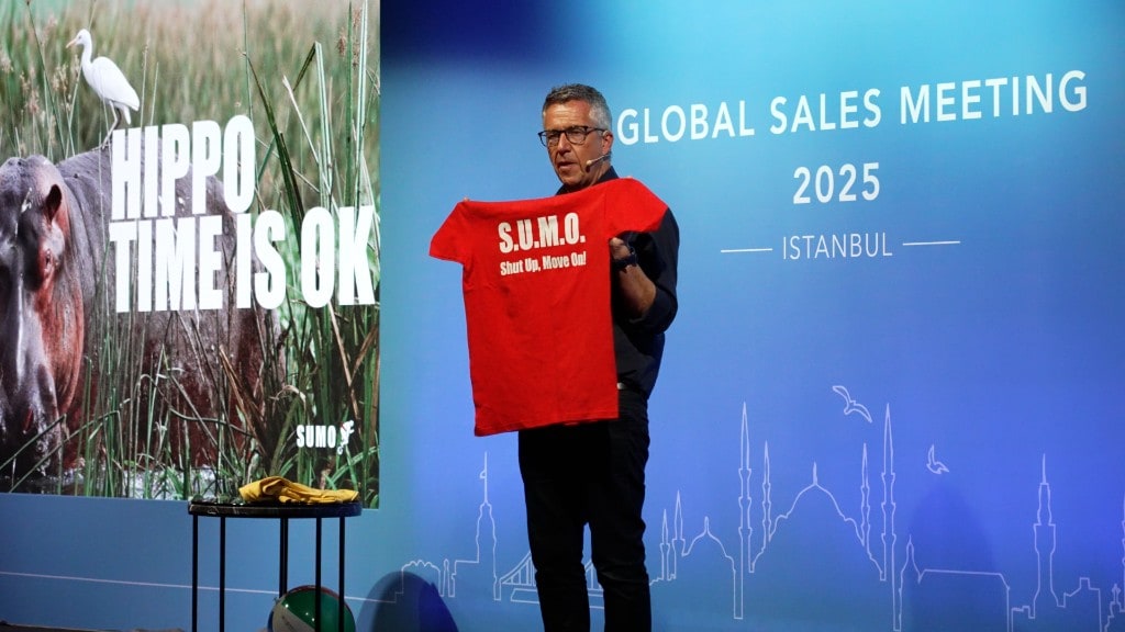Paul McGee on stage holding up a red SUMO t-shirt at a conference